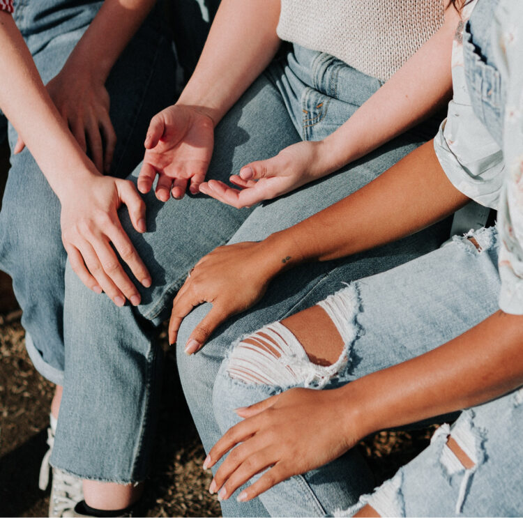 Woman touching another woman&#039;s leg supportively while they other two are talking