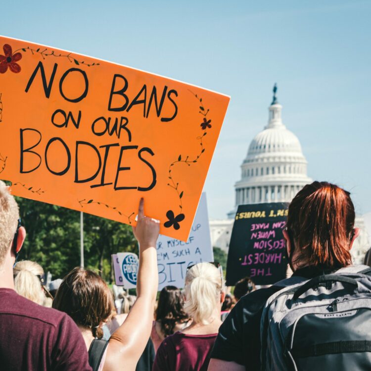 Protesters in front of the Capitol holding a no bans on our bodies sign