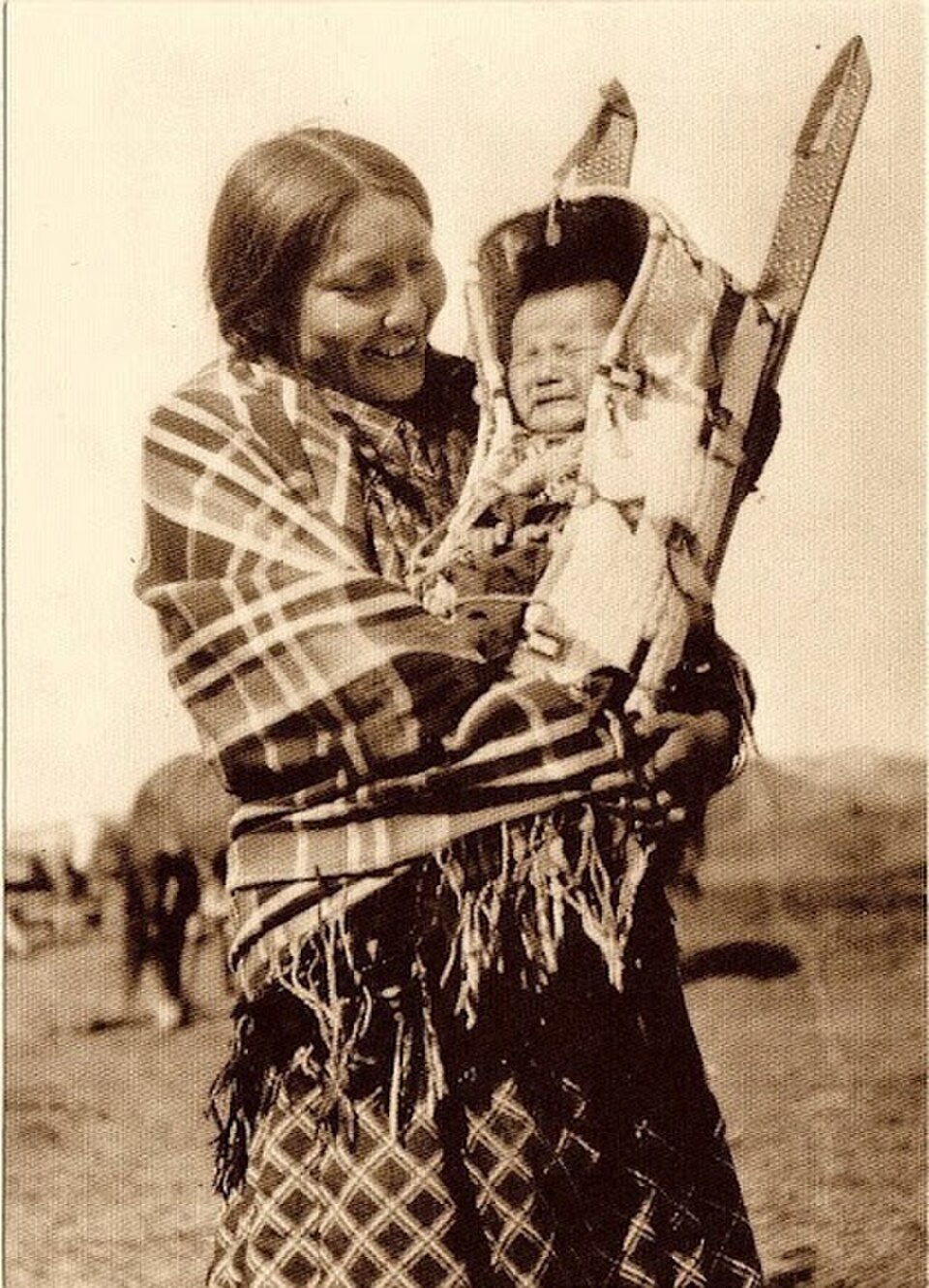 Native American smiling with child, using a traditional cradle board. P. 48 of The Kodak Book album. (Public Domain) 
